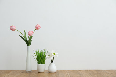 Beautiful flowers in vases and other floral decor on wooden table near white wall indoors, space for textの写真素材