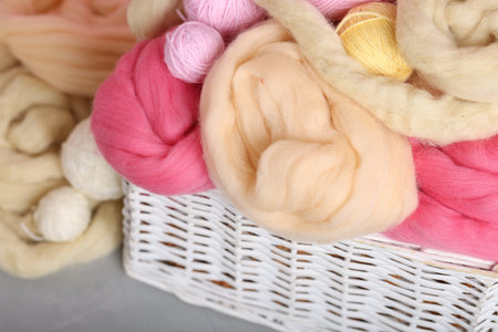 Soft felting wool and yarns in wicker basket on gray table, closeup