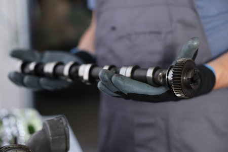 Auto part. Professional mechanic with camshaft indoors, closeup view