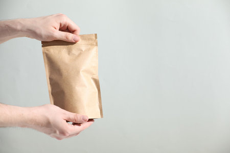Woman holding blank zipper stand-up pouch on light gray background, closeup. Space for text