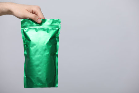 Woman holding blank zipper stand-up pouch on light gray background, closeup. Space for textの写真素材