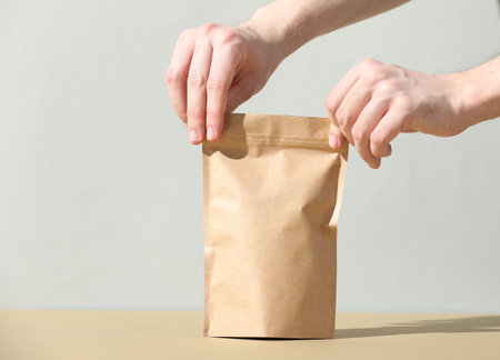 Woman holding blank zipper stand-up pouch on beige table against light gray background, closeup. Space for textの写真素材