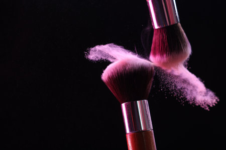 Makeup brushes with pink eye shadow on black background, closeup. Space for textの写真素材