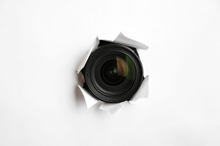 Hidden camera lens through torn hole in white paperの写真素材