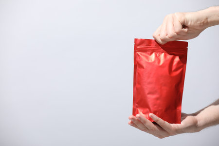 Woman holding blank zipper stand-up pouch on light gray background, closeup. Space for textの写真素材