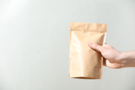 Woman holding blank zipper stand-up pouch on light gray background, closeup. Space for textの写真素材