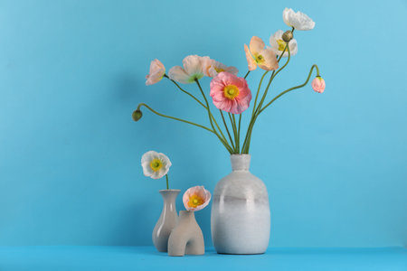 Beautiful poppy flowers in vases on light blue background, closeup