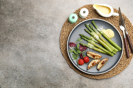 Tasty cooked asparagus served with baked potatoes, tomatoes and sauce on gray table, flat lay. Space for textの写真素材