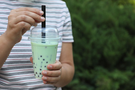 Woman with tasty milk bubble tea in plastic cup outdoors, closeup. Space for textの写真素材