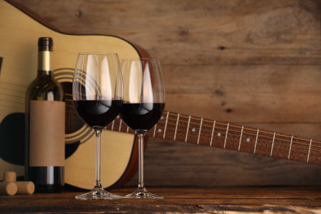 Acoustic guitar, bottle and glasses of red wine on wooden table. Space for textの写真素材