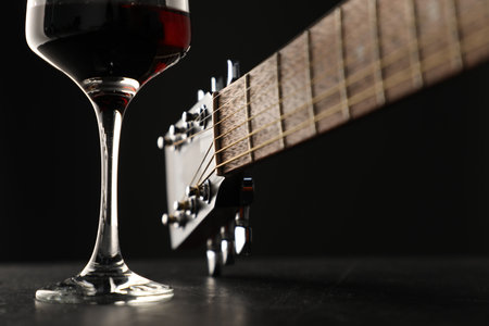 Acoustic guitar and glass of red wine on black table, closeupの写真素材