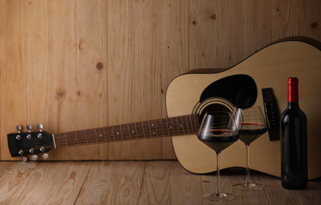 Acoustic guitar, bottle and glasses of red wine on wooden table. Space for textの写真素材