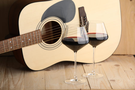 Acoustic guitar and glasses of red wine on wooden tableの写真素材