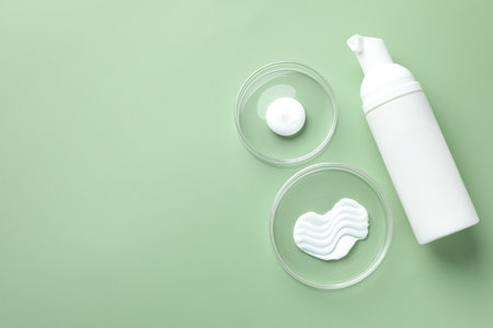 Different cosmetic products in Petri dishes and bottle on green background, flat lay. Space for textの写真素材