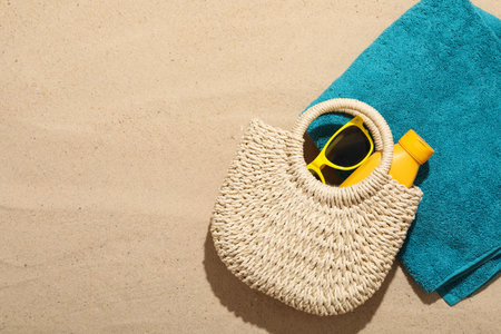 Beach towel, straw bag, sunscreen product and sunglasses on sand outdoors, flat lay. Space for textの写真素材
