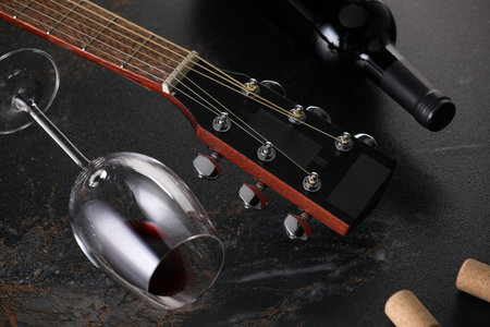 Acoustic guitar and red wine on black table, closeup