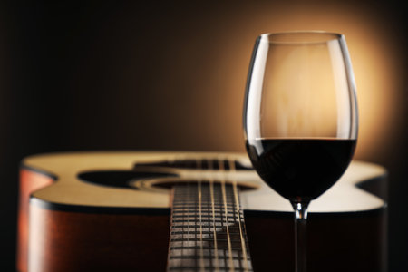 Acoustic guitar and glass of red wine on black background, closeup. Space for textの写真素材