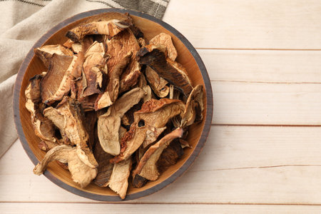 Pieces of dried mushrooms in bowl on light wooden table, top view. Space for textの写真素材