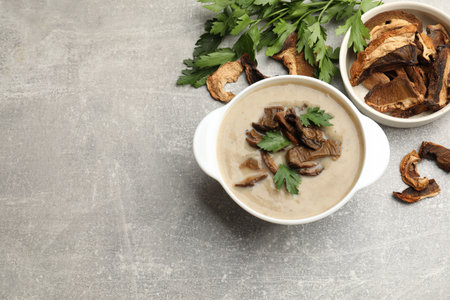 Tasty cream soup with mushrooms and parsley in bowl on gray textured table, flat lay. Space for textの写真素材