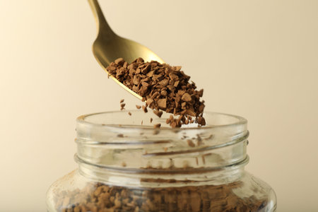 Taking instant coffee with spoon on beige background, closeup