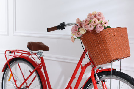 Bicycle with basket of beautiful flowers near white wall indoors, closeupの写真素材
