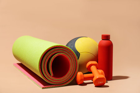 Medicine ball, dumbbells, fitness mat and water bottle on beige backgroundの写真素材