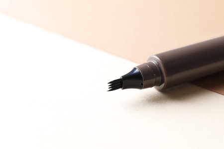 Brown liquid eyebrow pencil on beige background, closeup. Space for text
