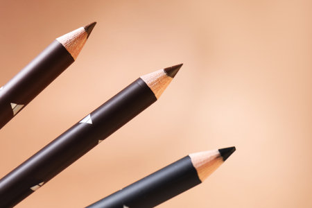 Different eyebrow pencils on beige background, closeup. Space for textの写真素材