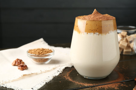 Delicious dalgona coffee in glass, granules, walnuts and brown sugar on wooden table, closeupの写真素材