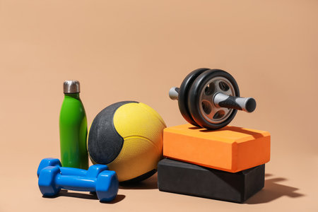 Medicine ball, foam blocks, dumbbells, ab wheel and water bottle on beige backgroundの写真素材