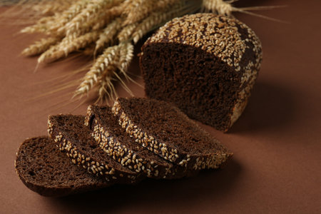 Fresh rye bread with seeds and spikes on brown background, closeup