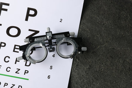 Vision test chart and trial frame on grey table, top view. Space for text