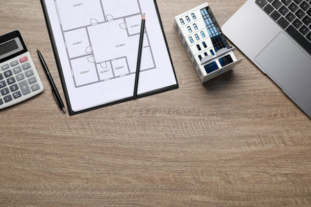 Real estate. Apartment building model, floor plan, calculator and laptop on wooden table, flat lay....