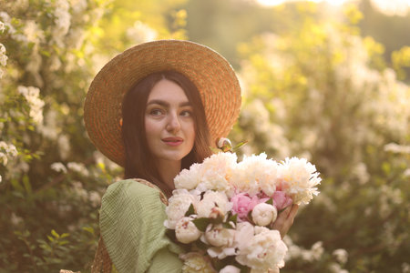 Beautiful woman with bouquet of peonies in park on sunny dayの写真素材