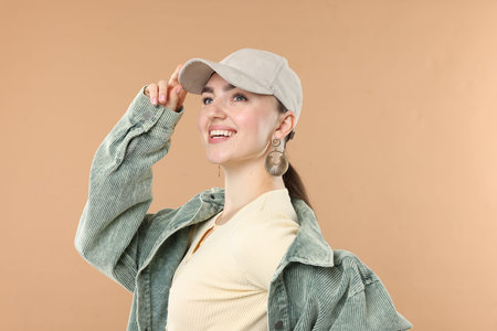Smiling woman in stylish baseball hat on beige backgroundの写真素材
