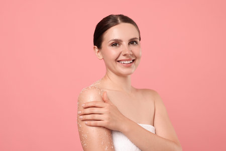 Smiling woman applying body scrub onto her arm against pink backgroundの写真素材