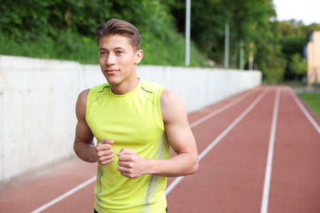 Sporty man running at stadium, space for text. Healthy lifestyle