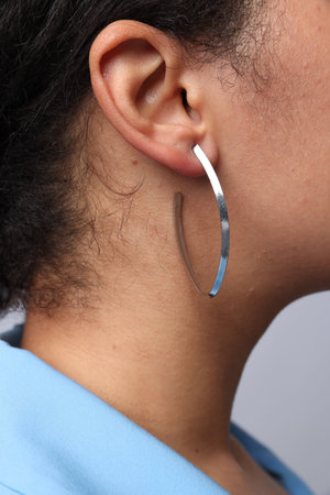 Young woman wearing elegant silver earring on light grey background, closeup