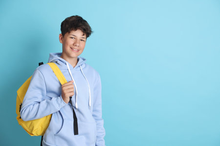 Teenage boy with backpack on light blue background, space for text