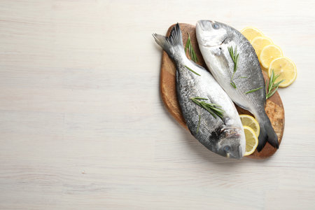 Organic seafood. Fresh raw dorado fish, lemon slices and rosemary on white wooden table, flat lay. Space for textの写真素材
