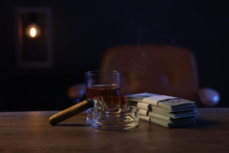 Ashtray with cigar, money and whiskey on wooden table in mafia boss office