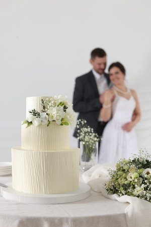 Happy married couple together indoors, focus on wedding cake and bouquet on tableの写真素材