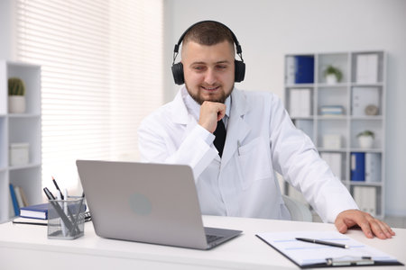 Doctor in headphones having online consultation via laptop indoorsの写真素材