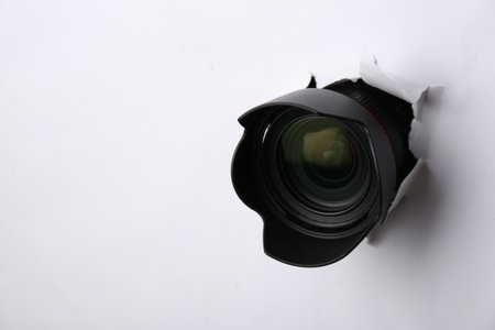 Hidden camera lens through torn hole in white paper. Space for textの写真素材