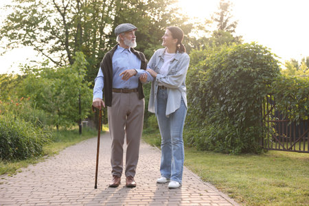 Smiling caregiver supporting elderly man with walking cane outdoors
