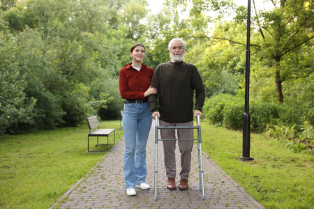 Smiling caregiver supporting elderly man who using walking frame outdoors