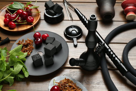Traditional hookah parts, tobacco, charcoal cubes, cherries and mint on wooden table