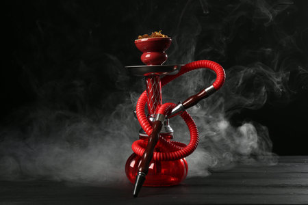 Hookah on wooden table with smoke against black background