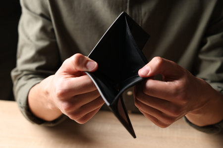Man with empty wallet at wooden table, closeup