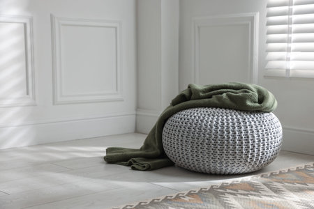 Stylish knitted pouf with plaid at home. Space for textの写真素材